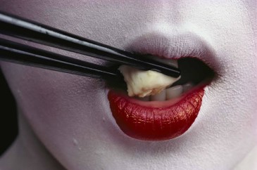 Close view of a geisha eating tofu with chopsticks.